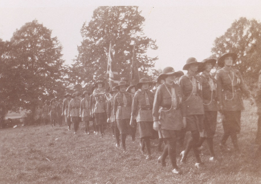girls from the Walton Girl Guides hiking with the Union Jack at camp in 1928.