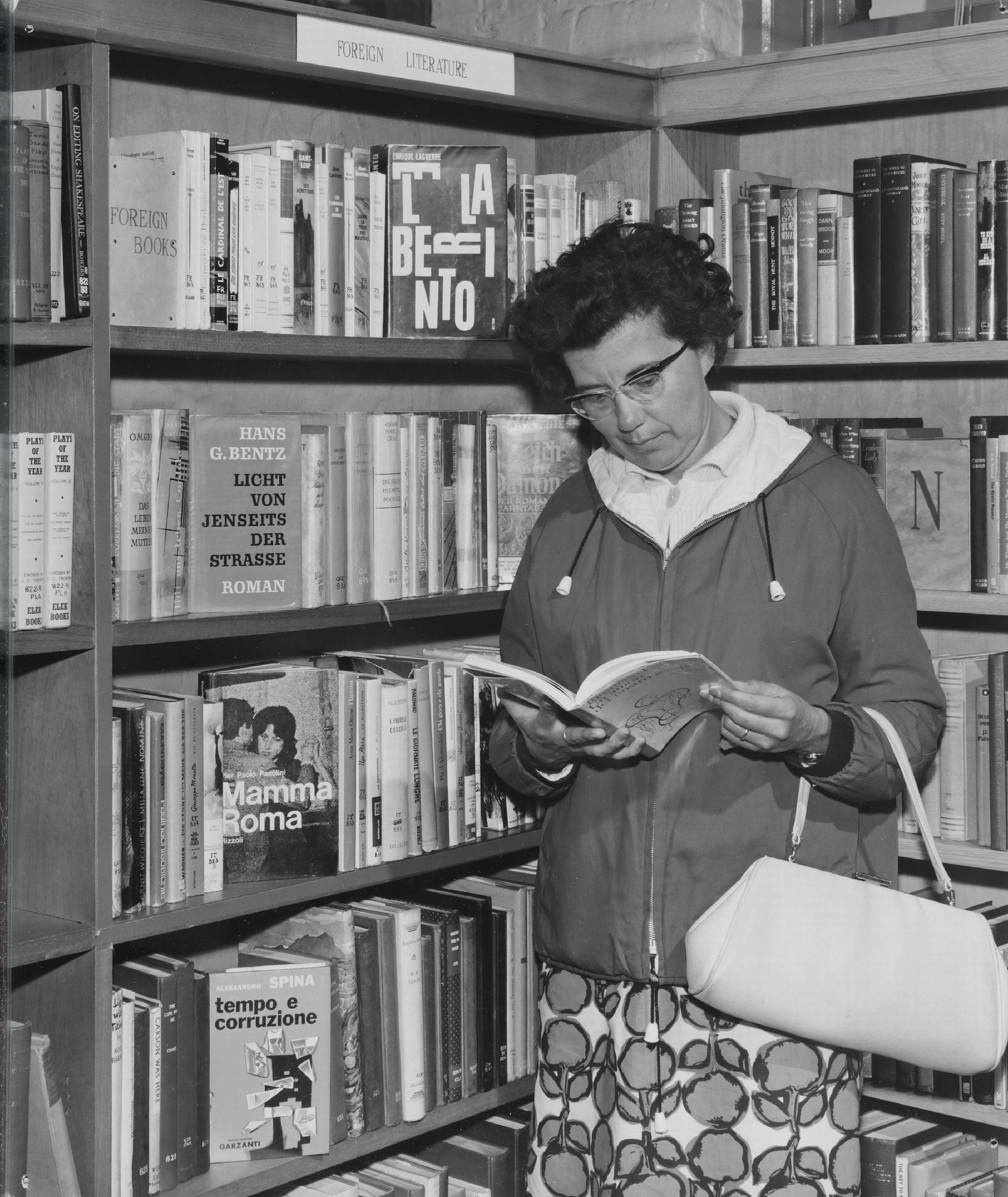 Interior of Walton Library, showing a member of the public looking at a book in a foreign language in front of a bookcase labelled 