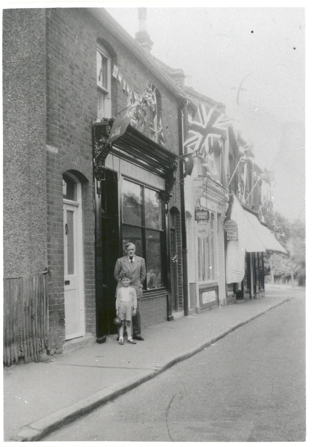 Henry Hibbert (b.1884, d.1975) and grandson, Charles Hibbert, outside Hibbert's greengrocers, Claygate, during the coronation of Queen Elizabeth II, June 1953