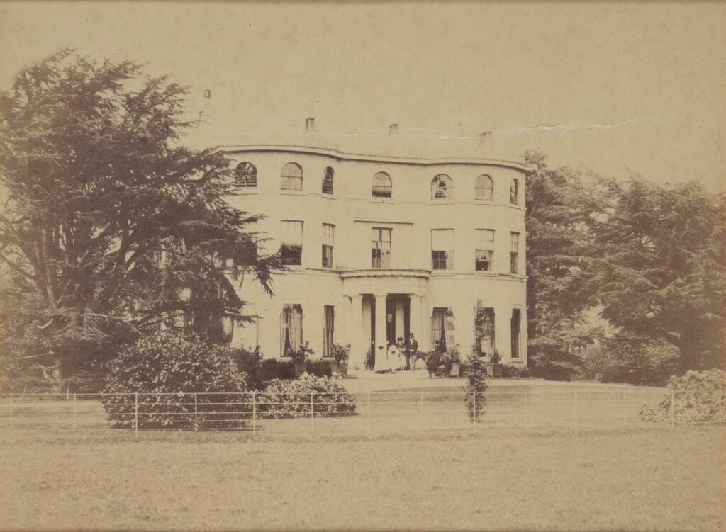 A photograph of the front face of Apps Court, with the Gill family gathered on the steps at the front entrance.