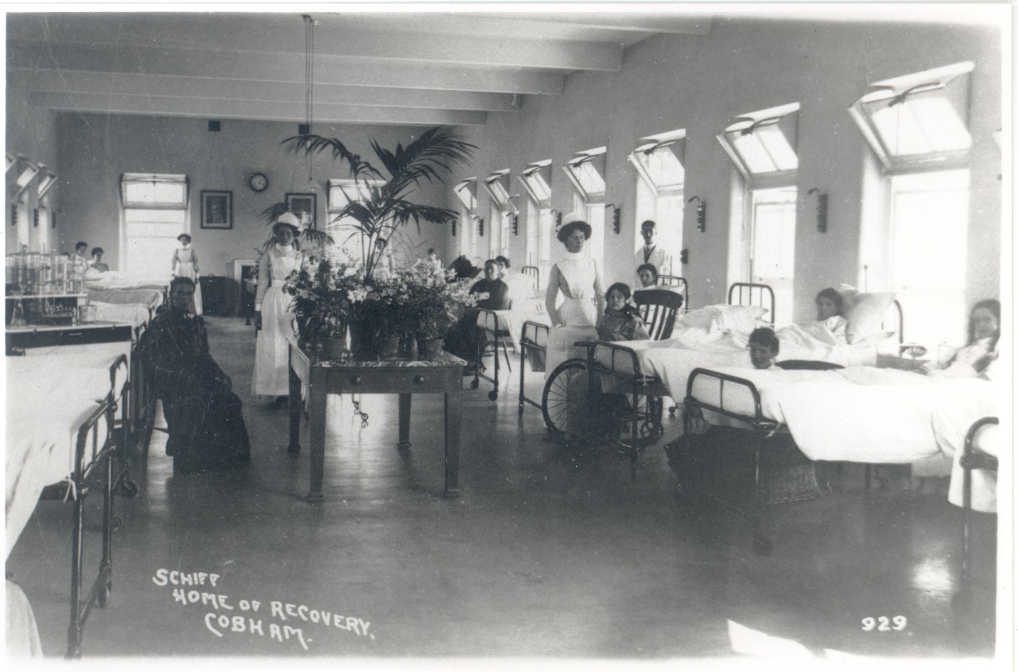 Postcard of the Schiff Home of Recovery, Cobham, showing interior of ward with adults and children, nurses and a doctor.