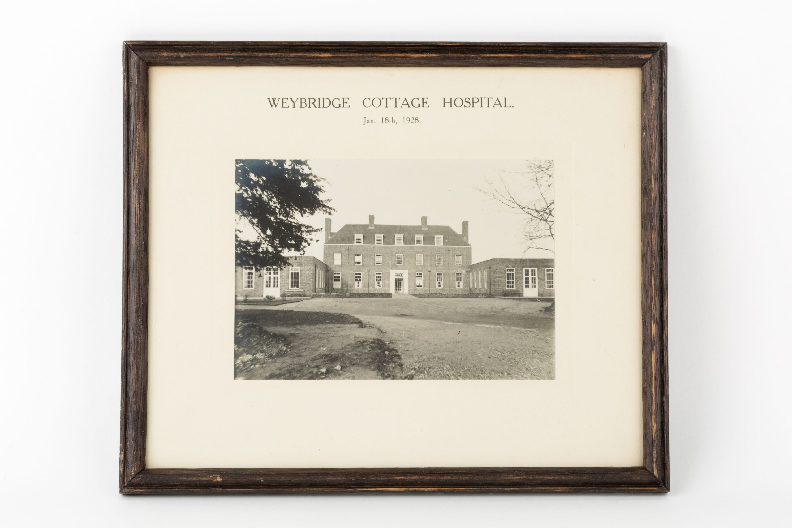 Framed black and white photograph of the front view of the new Weybridge Cottage Hospital, Church Street, 1928. It was donated by a nurse who worked at the hospital during the Second World War. Undated but post-1928.