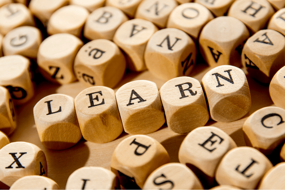 An image of wooden dice with letters printed on them. 5 dice are arranged in the centre of the image spelling the word 'learn'.